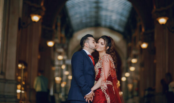 Beautiful woman in a long red dress walks around the city with her husband in a blue suit and with a beard